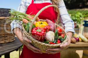 Mid section of woman holding a basket of fresh vegetables at stall