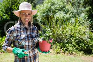 Portrait of happy woman holding sapling and trowel in garden
