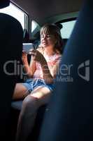 Teenage girl in headphones using mobile phone in the back seat of car