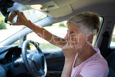 Senior woman looking into rear view mirror while driving a car