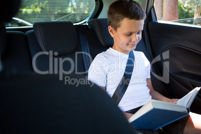 Teenage boy reading book in the back seat of car