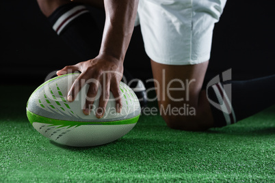 Side view of sportsman kneeling while holding rugby ball