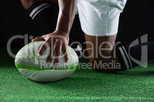 Side view of sportsman kneeling while holding rugby ball