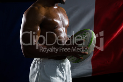 Mid section of shirtless sportsman holding rugby ball against Italian Flag