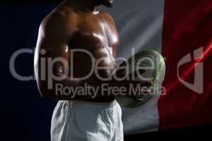 Mid section of shirtless sportsman holding rugby ball against Italian Flag