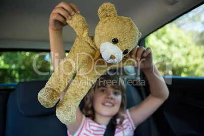 Teenage girl playing with teddy bear in back seat of car