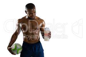 Shirtless sportsman with rugby ball holding drinking bottle