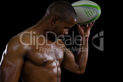 Shirtless male athlete flexing muscles while holding rugby ball