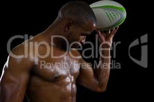 Shirtless male athlete flexing muscles while holding rugby ball