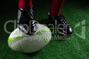 Low section of sportsperson stepping on rugby ball