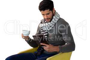 Man using digital tablet while having cup of tea