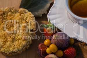 Various fruits, sweet food, and cup of green tea on chopping board