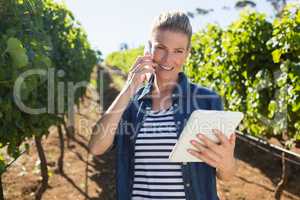 Female vintner using digital tablet while talking on mobile phone