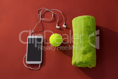 Overhead view of tennis ball amidst napkin and mobile phone with in-ear headphones