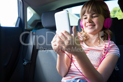 Teenage girl in headphones using digital tablet in the back seat of car