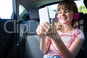 Teenage girl in headphones using digital tablet in the back seat of car