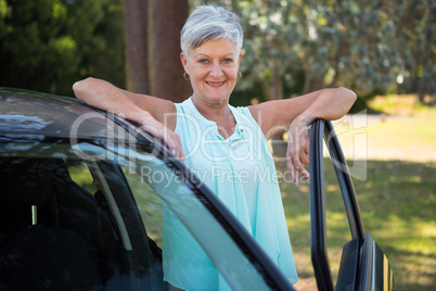 Senior woman standing beside a car