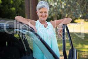 Senior woman standing beside a car