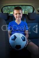 Happy teenage boy sitting with football in the back seat of car