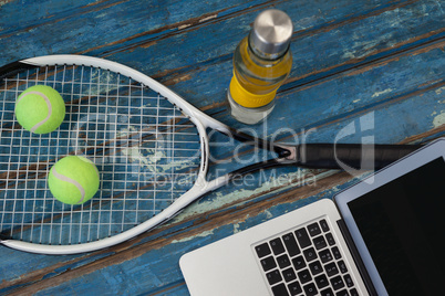 High angle view of laptop by tennis racket and balls with water bottle