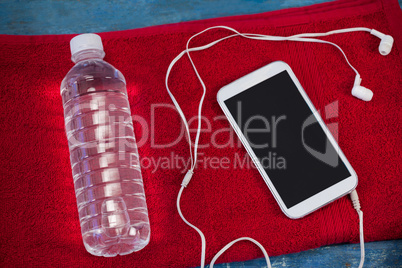 High angle view of water bottle and mobile phone with in-ear headphones on red napkin