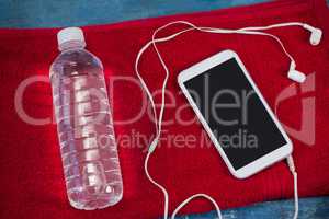 High angle view of water bottle and mobile phone with in-ear headphones on red napkin