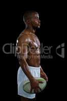 Side view of shirtless athlete with rugby ball looking away