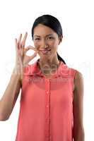 Smiling woman gesturing okay hand sign against white background