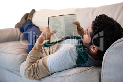 Man lying on sofa while reading book