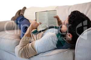 Man lying on sofa while reading book