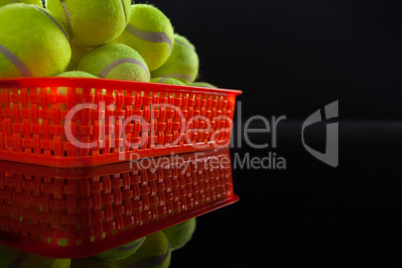 Pile of fluorescent yellow tennis balls in red plastic basket with reflection