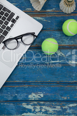 Overhead view of laptop and eyeglasses with shuttlecocks by tennis balls