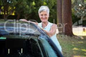 Senior woman standing beside a car