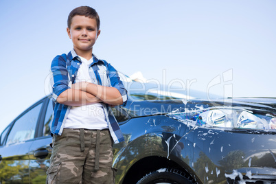 Teenage boy standing with arms crossed near a car