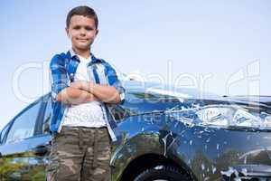 Teenage boy standing with arms crossed near a car