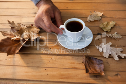 Man having a cup of black coffee with autumn leaves on wooden table