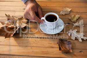 Man having a cup of black coffee with autumn leaves on wooden table
