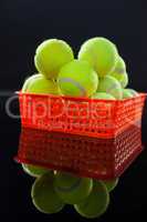 Close up of tennis balls in red plastic basket with reflection