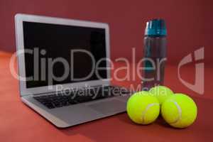Close up of tennis balls by laptop and water bottle