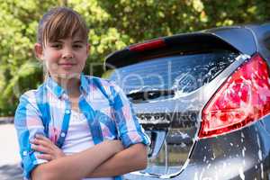 Teenage girl standing with arms crossed near a car