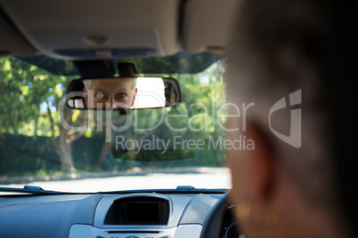 Senior woman looking into rear view mirror while driving a car