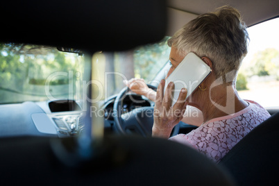 Senior woman talking on mobile phone while driving a car