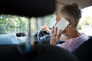Senior woman talking on mobile phone while driving a car