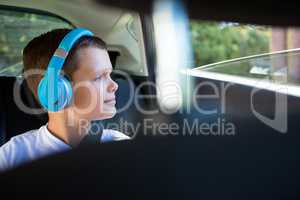 Teenage boy with headphones sitting in the back seat of car