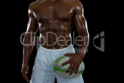 Mid section of shirtless male athlete holding rugby ball
