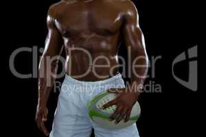 Mid section of shirtless male athlete holding rugby ball