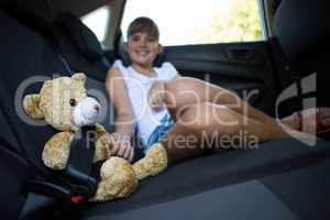 Teenage girl sitting with teddy bear in the back seat of car