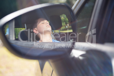 Reflection of teenage boy in wing mirror sleeping in car