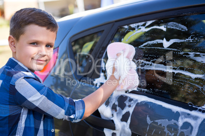 Teenage boy washing a car on a sunny day