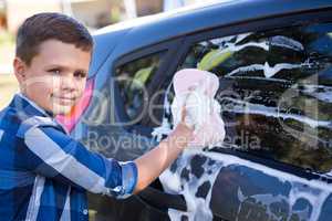 Teenage boy washing a car on a sunny day